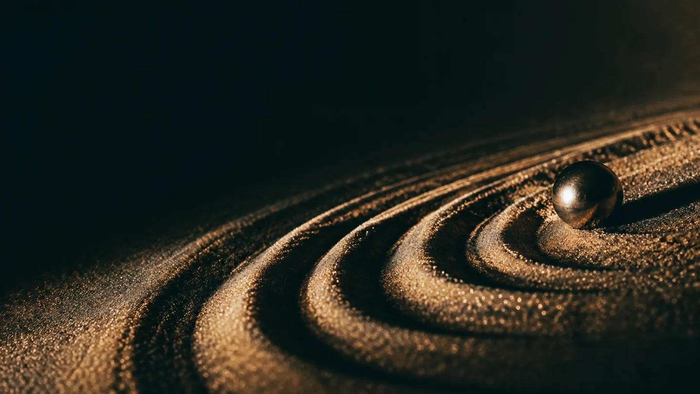 Golden light grazing flowing grooves in sand around a polished sphere
